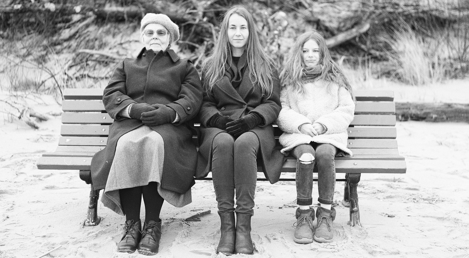 Mother in between Grandma and Daughter Sitting on a bench
